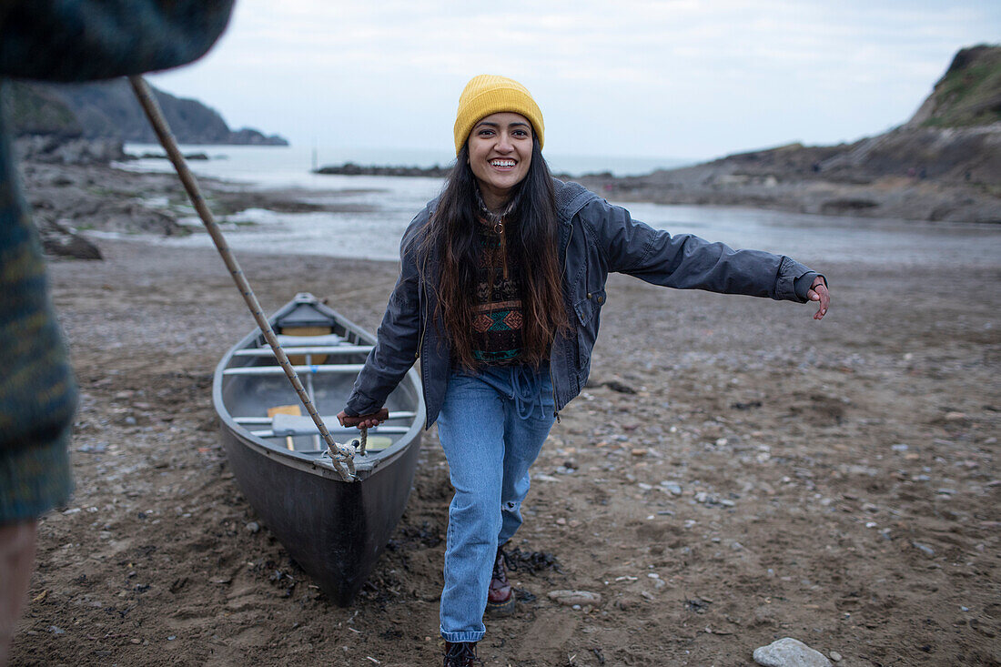 Happy young woman pulling canoe on beach