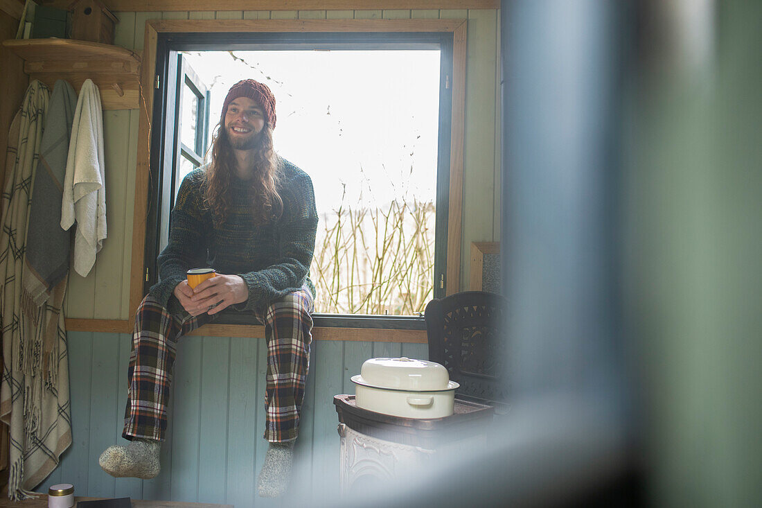Happy young man in pyjamas enjoying coffee in cabin window