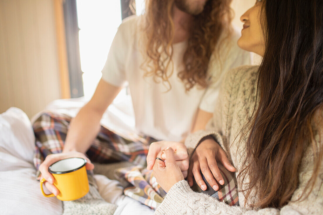 Affectionate young couple with coffee holding hands in bed