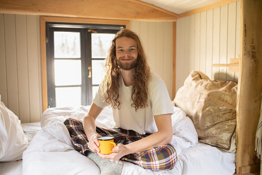 Happy young man in pyjamas drinking coffee in bed