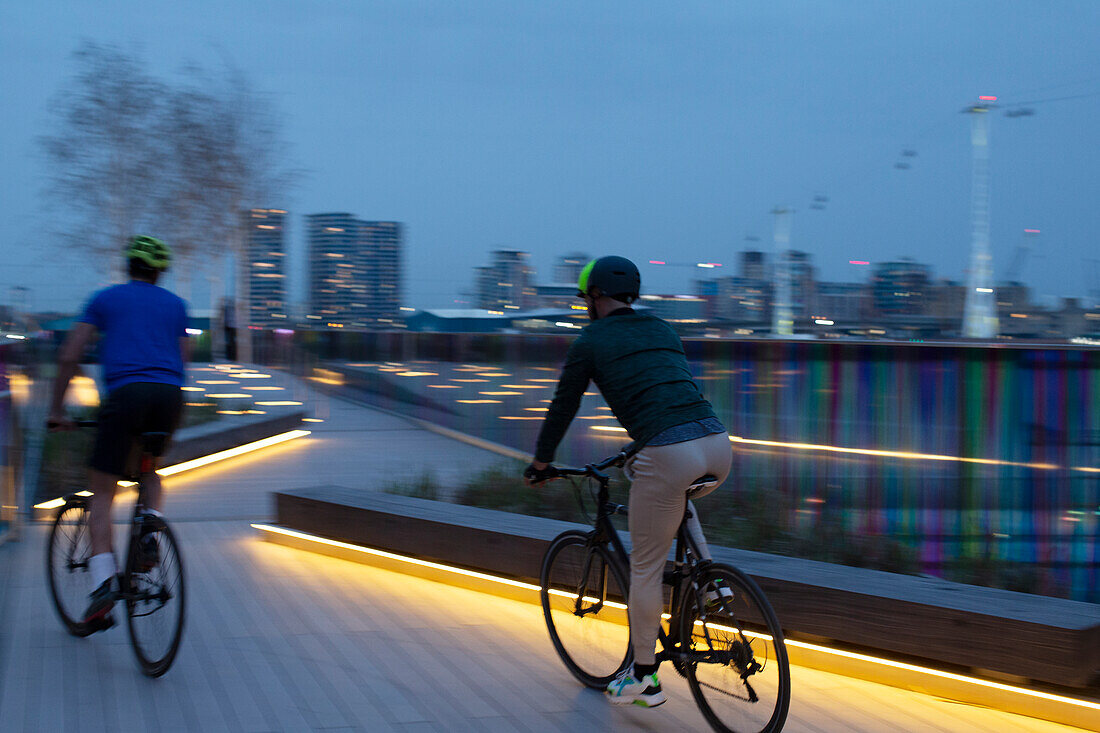 Men riding bicycles on boardwalk in city at night