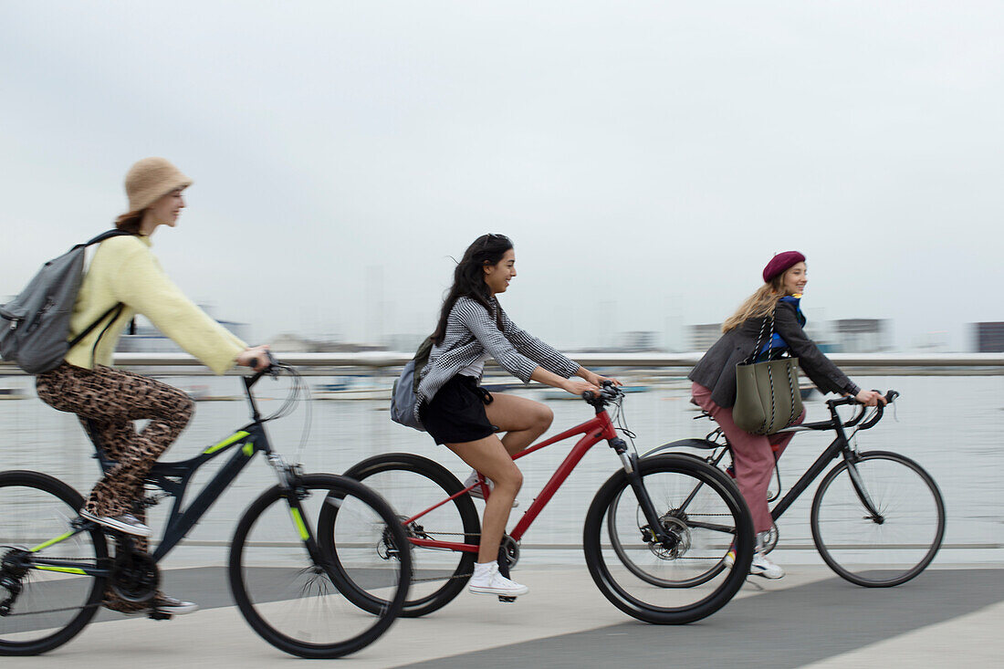 Young female friends riding bicycles along waterfront