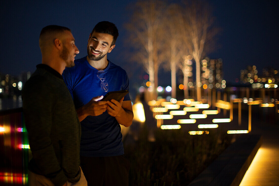 Happy men using digital tablet in city park at night