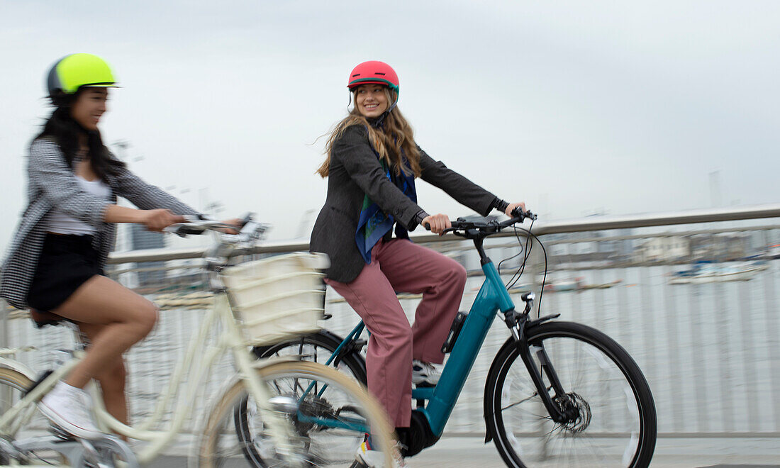 Happy young female friends riding bicycles on urban bridge