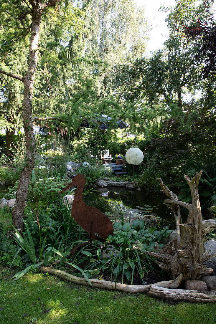 Decoration made with rusted metal and driftwood at a pond in the lush garden