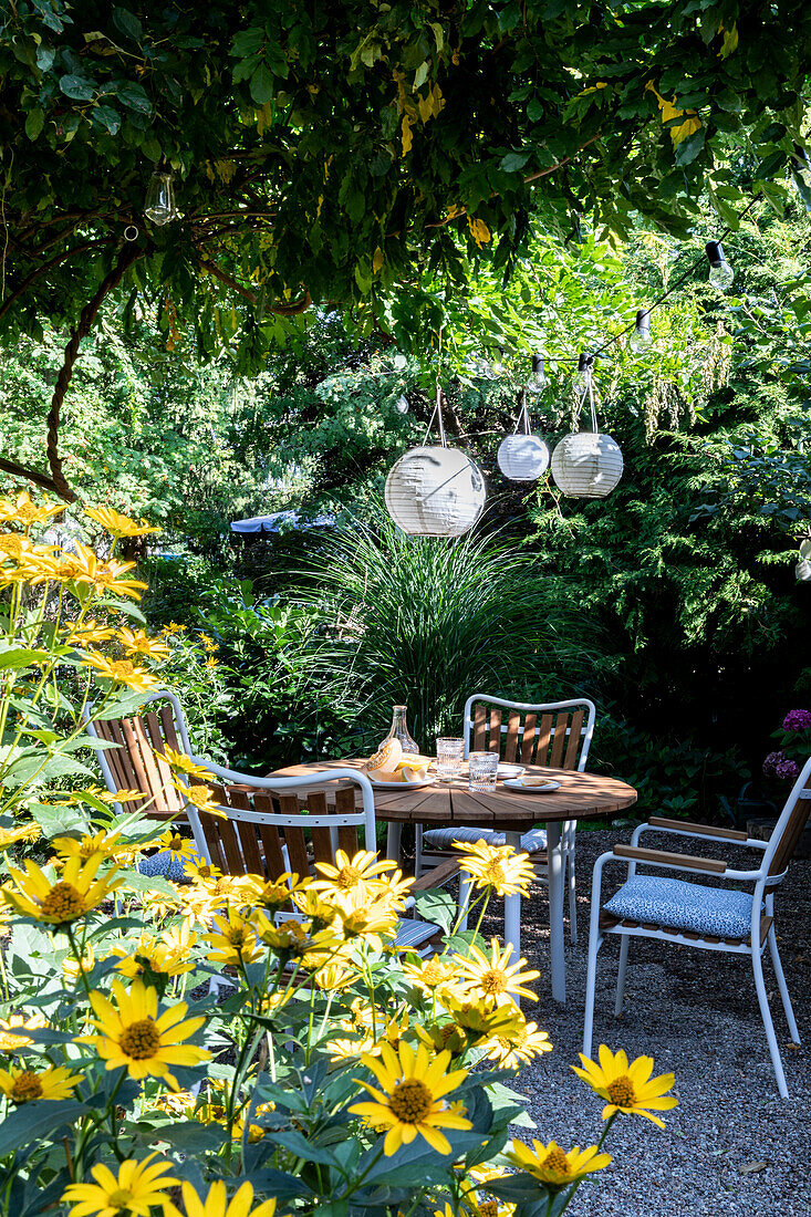 Runder Tisch mit Stühlen auf Kiesplatz, darüber Laternen im Garten