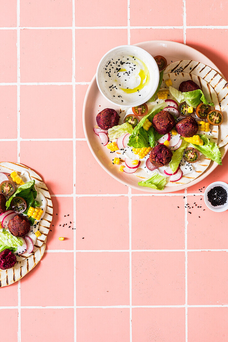 Rote-Bete-Falafel mit Mais, Tomaten, Rettich, Feta und schwarzem Sesam auf Fladenbrot