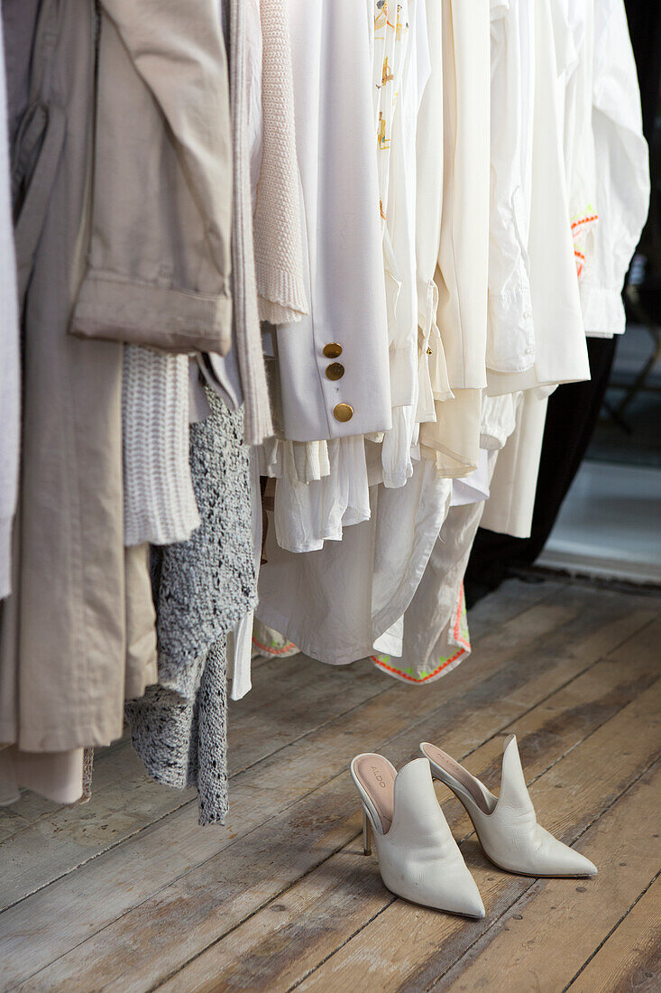 Clothes on a coat rack and white stilettos on a wooden floor