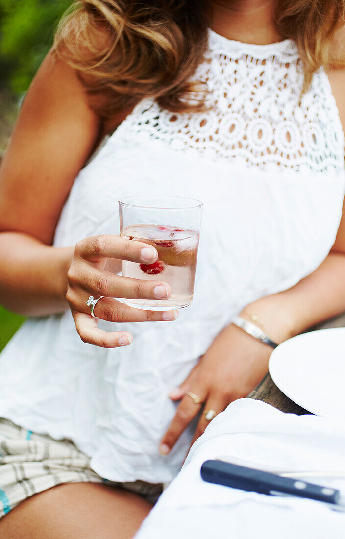 Frau in Sommerkleidung hält ein Glas Spritzer mit Rosé-Wein und Wodka