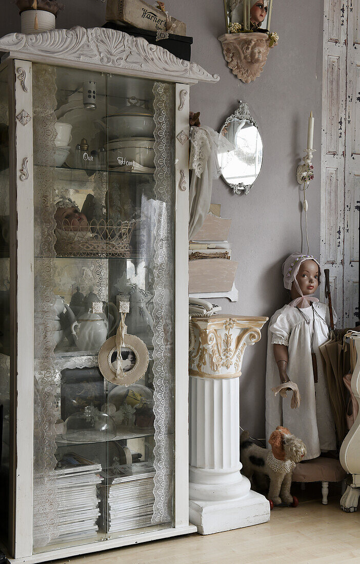 Old glass cabinet with dishes and magazines, doll in the background