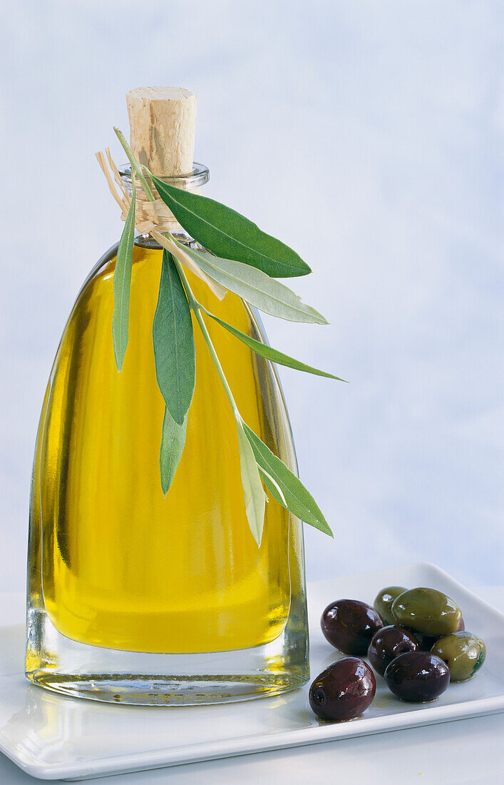 Flasche Olivenöl mit Olivenzweig, daneben einige Oliven