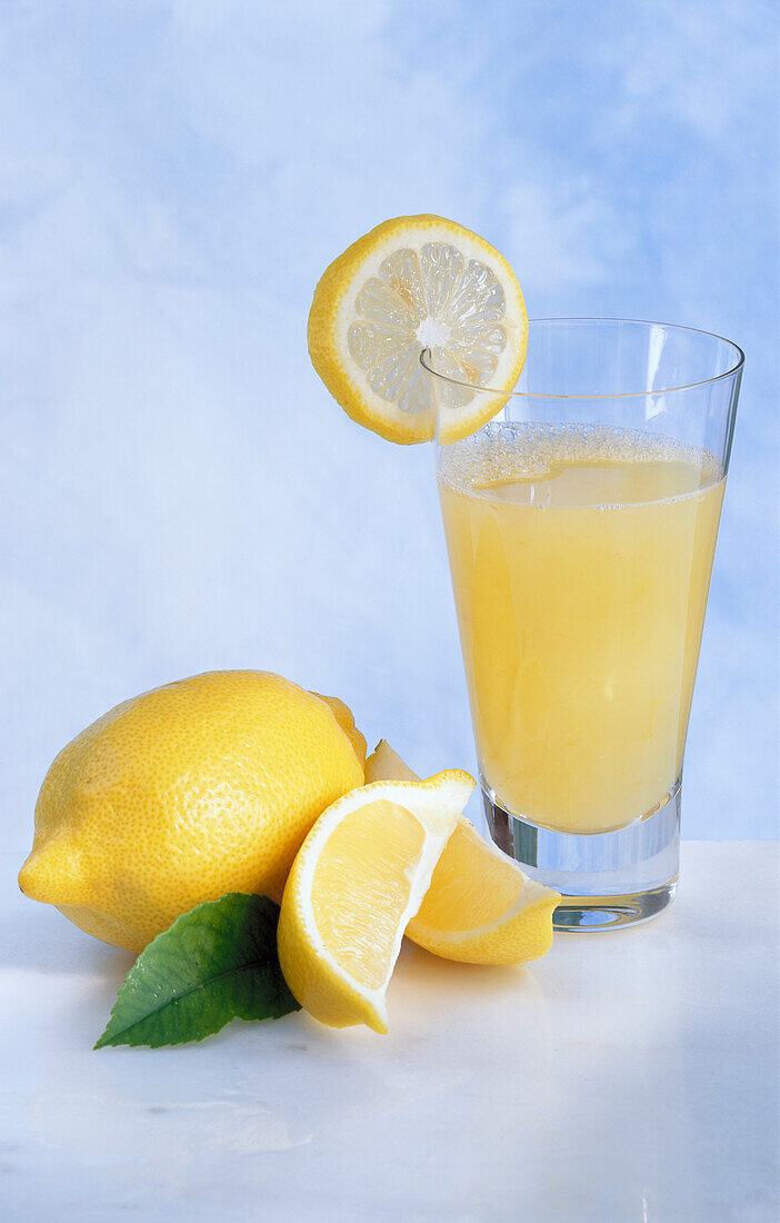 Glas mit Zitronensaft, davor einige Zitronen