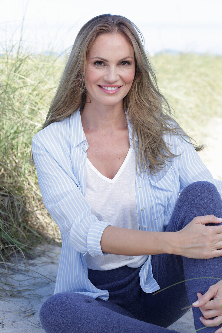 Long-haired woman in spring-like blue and white outfit sitting on the beach