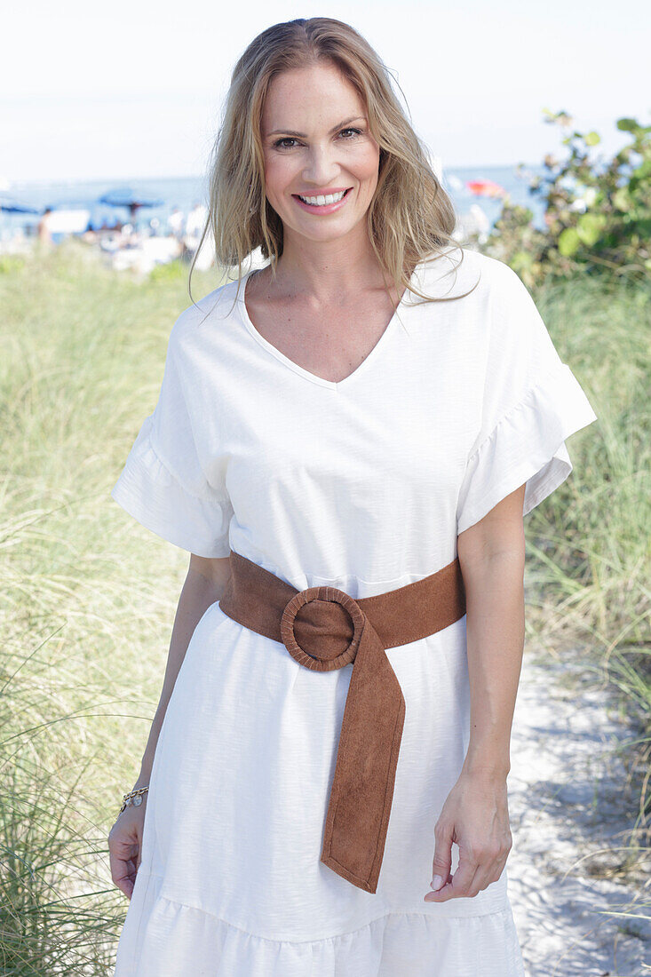 Langhaarige Frau in weißem Sommerkleid mit Gürtel am Strand