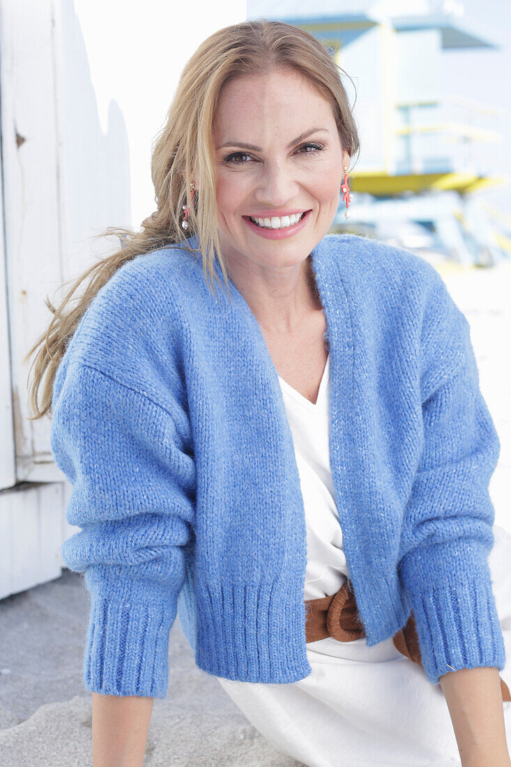 Langhaarige Frau in weißem Sommerkleid und blauer Strickjacke am Strand