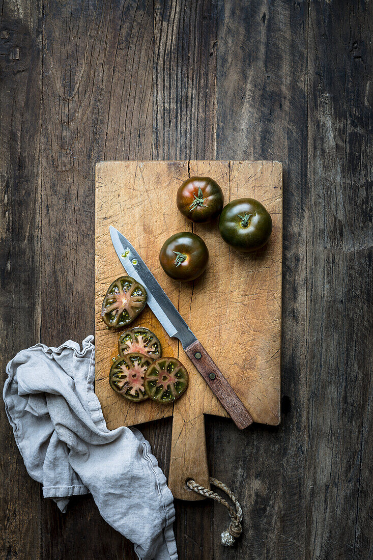 Whole and sliced green tomatoes on a rustic wooden chopping board