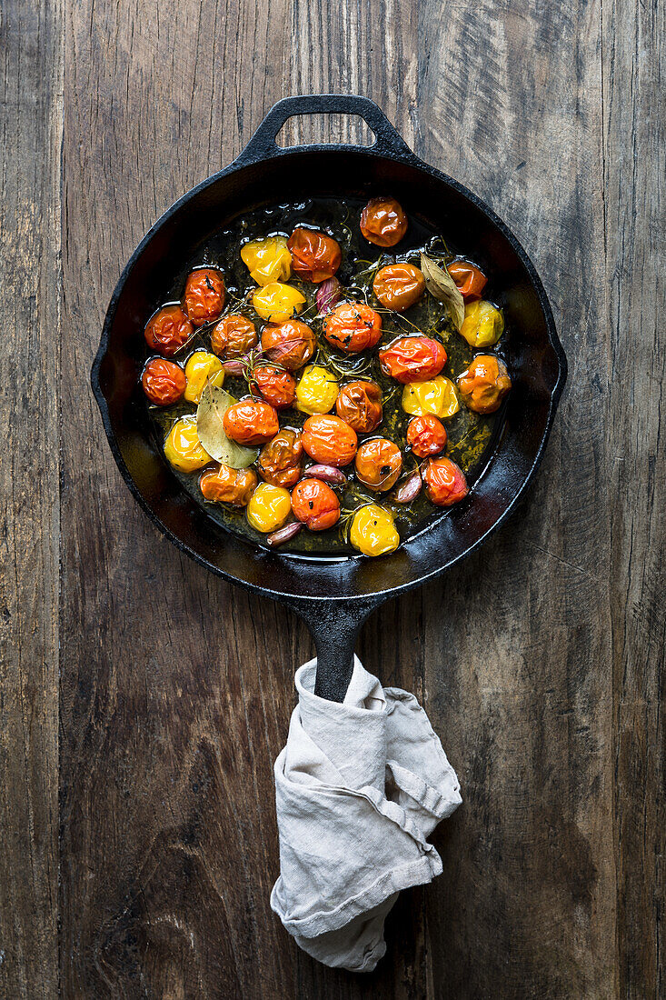 Roasted mixed varieties of tomatoes in a skillet with thyme, rosemary, garlic cloves, bay leaves