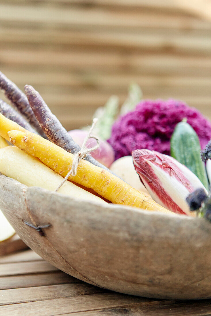 Colorful carrots and vegetables in a rustic wooden bowl on a wooden table