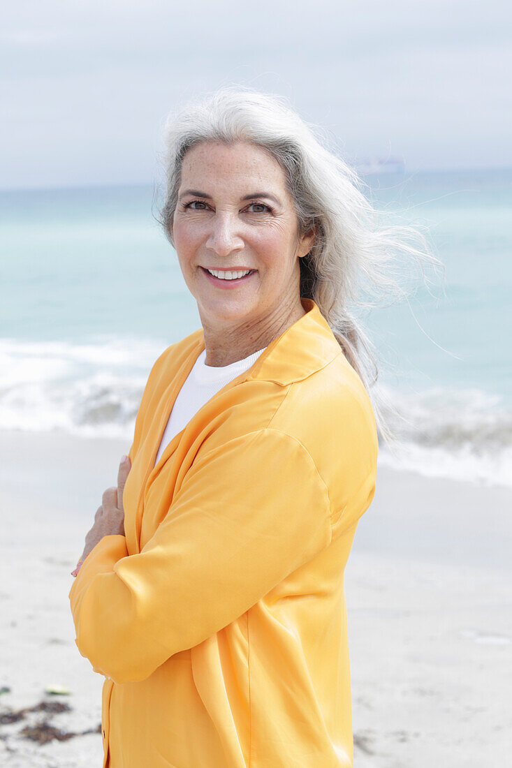 Mature woman with grey hair in orange blouse sitting on the beach