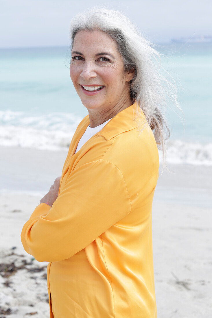 Reife Frau mit grauen Haaren in orangefarbener Bluse am Strand