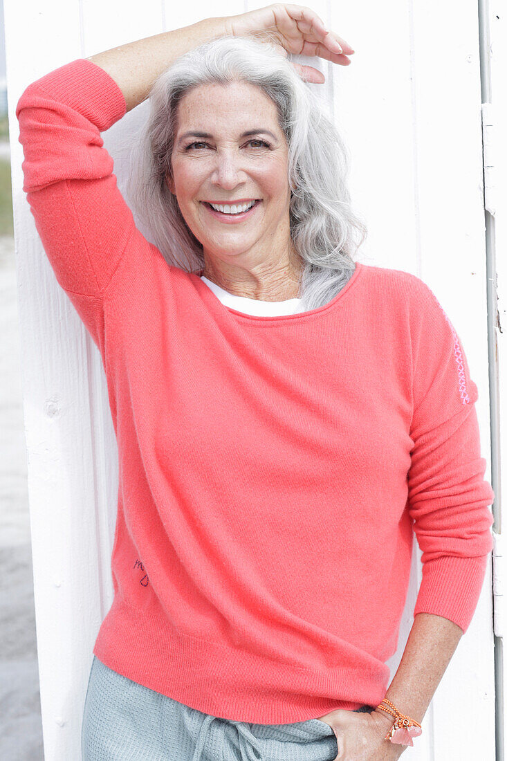 Reife Frau mit grauen Haaren in lachsfarbenem Pullover