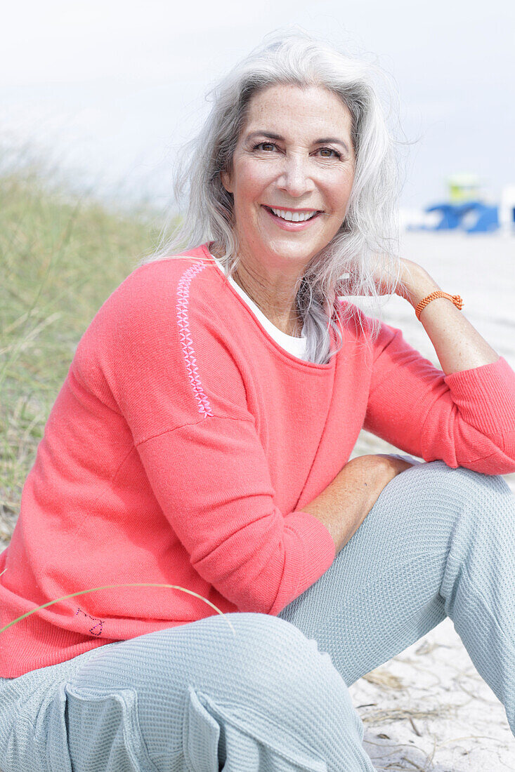 Mature woman with grey hair in salmon-coloured jumper and trousers on the beach