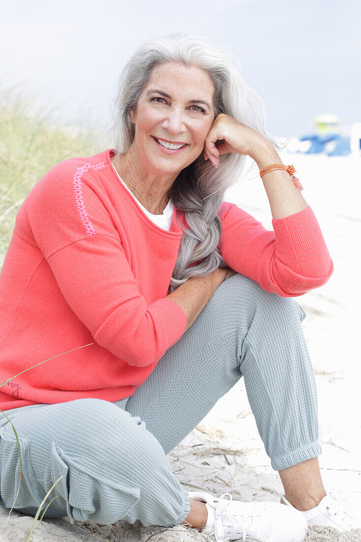 Mature woman with grey hair in salmon-coloured jumper and trousers on the beach