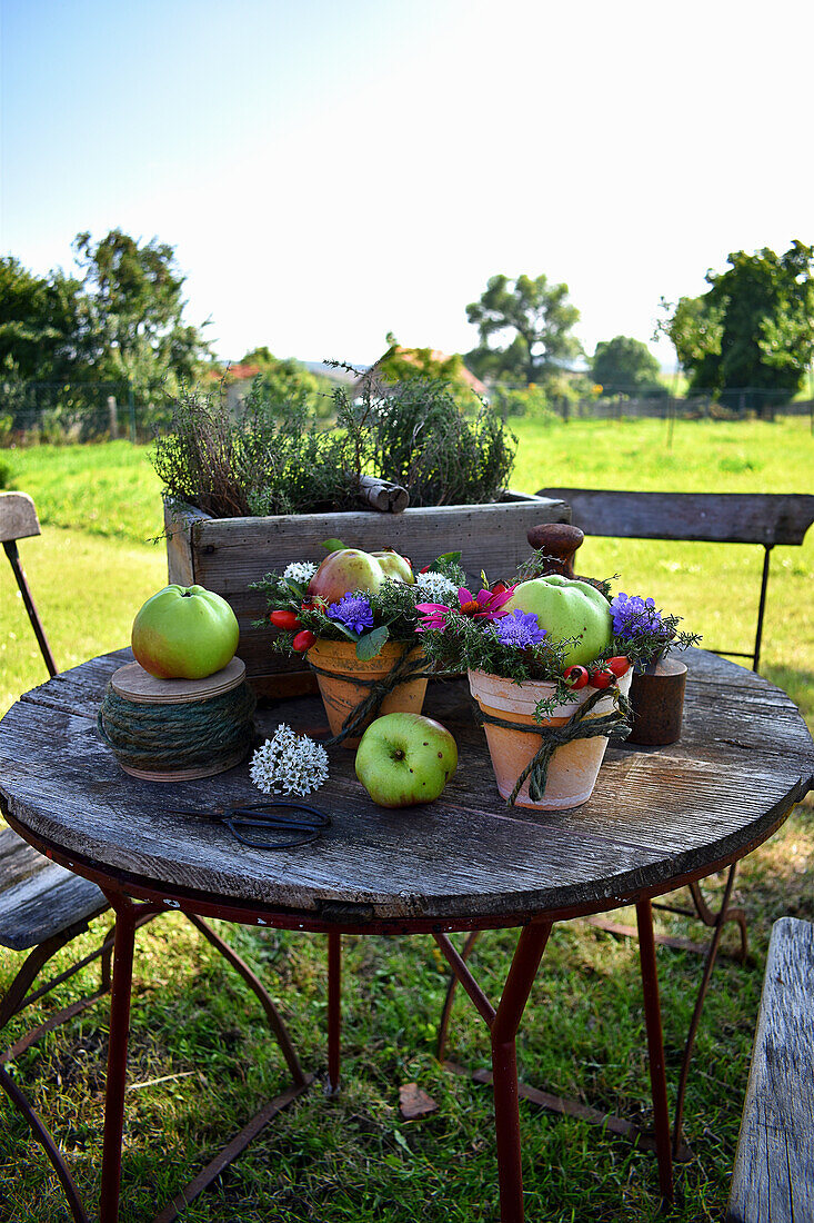Blumengesteck mit Apfel in Blumentöpfen auf Gartentisch