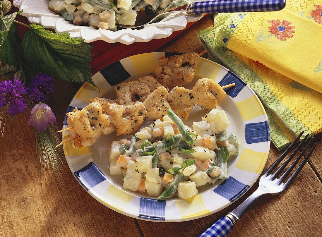 Potato salad with vegetables on plate with two poultry kebabs