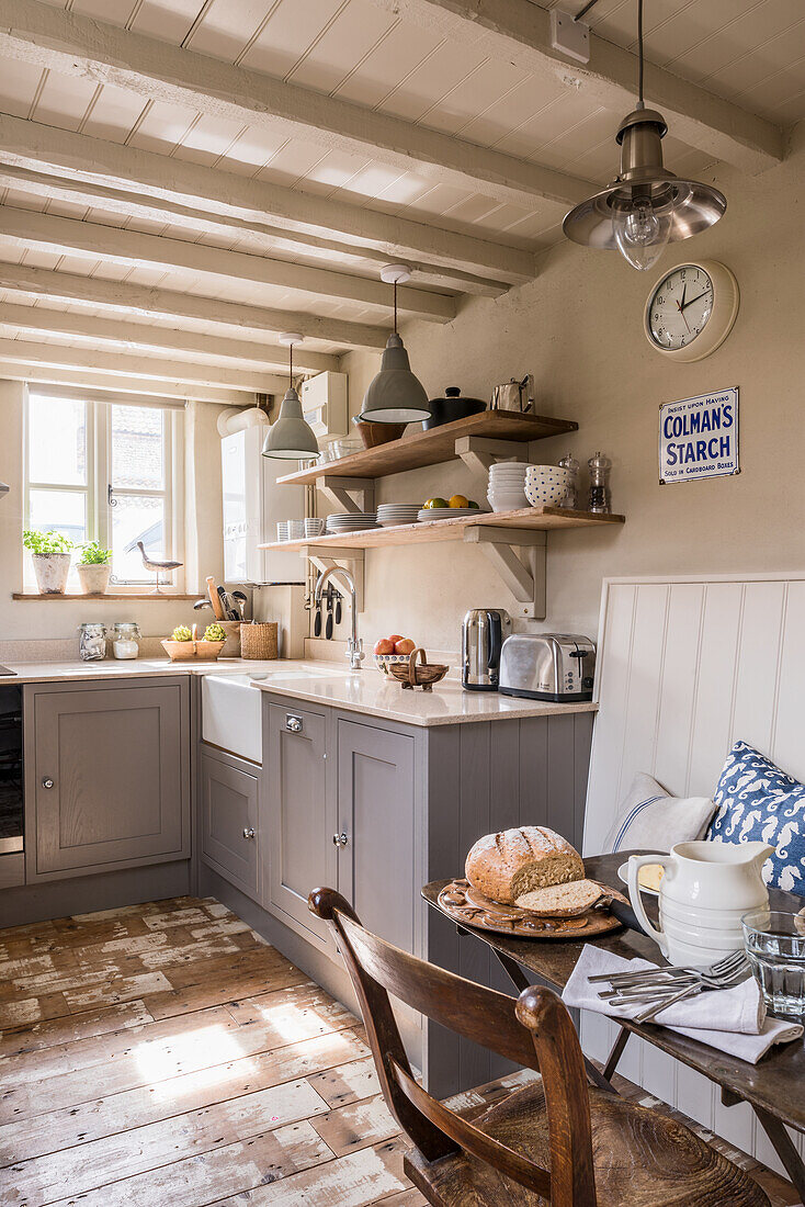 Country kitchen with grey cabinets, vintage pendant lights and covered dining table