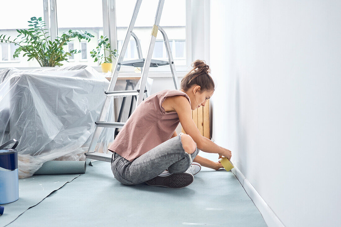 Junge Frau, die sitzend Klebeband an der Wand anbringt