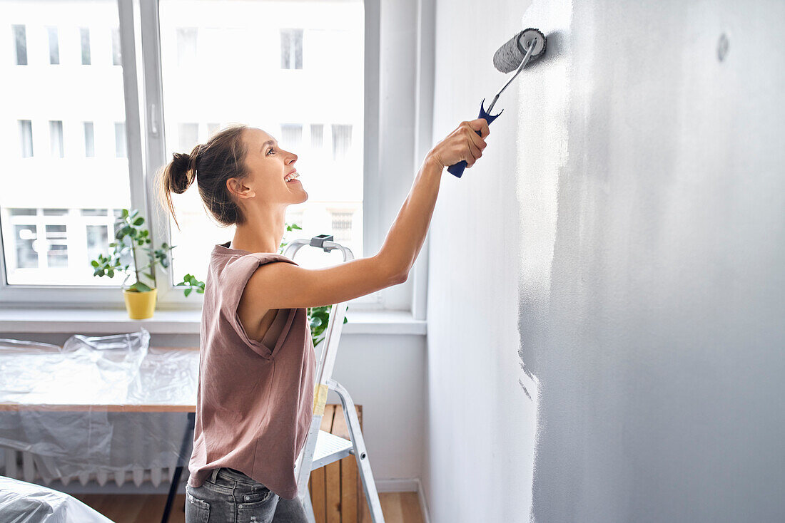 Smiling woman painting wall with paint roller