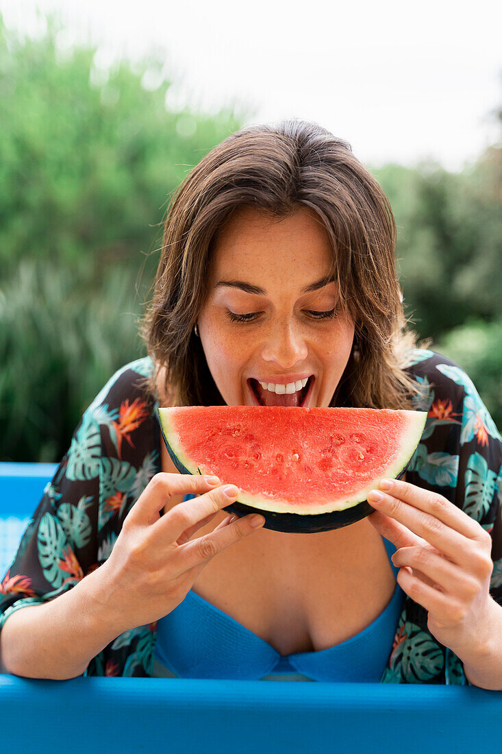 Glückliche junge Frau, die Wassermelone im aufblasbaren Swimmingpool am Hof isst
