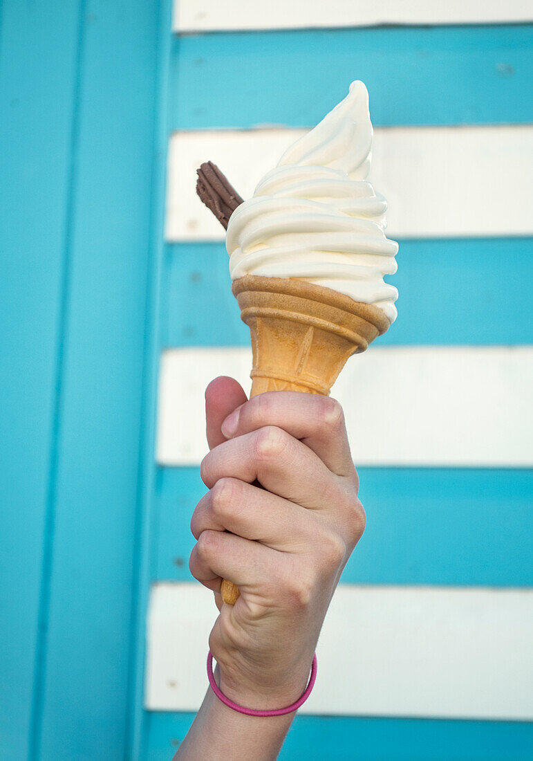Close-up of girl's hand holding ice cream cone against striped wall