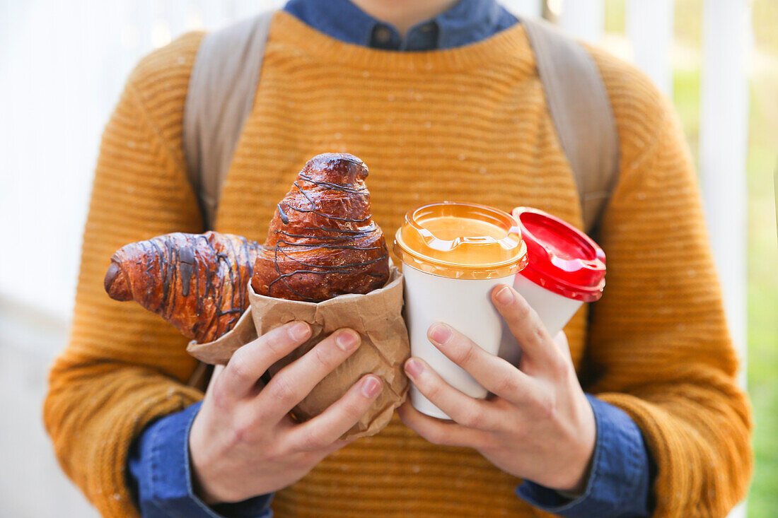 Junger Mann mit Croissant und Kaffee zum Mitnehmen