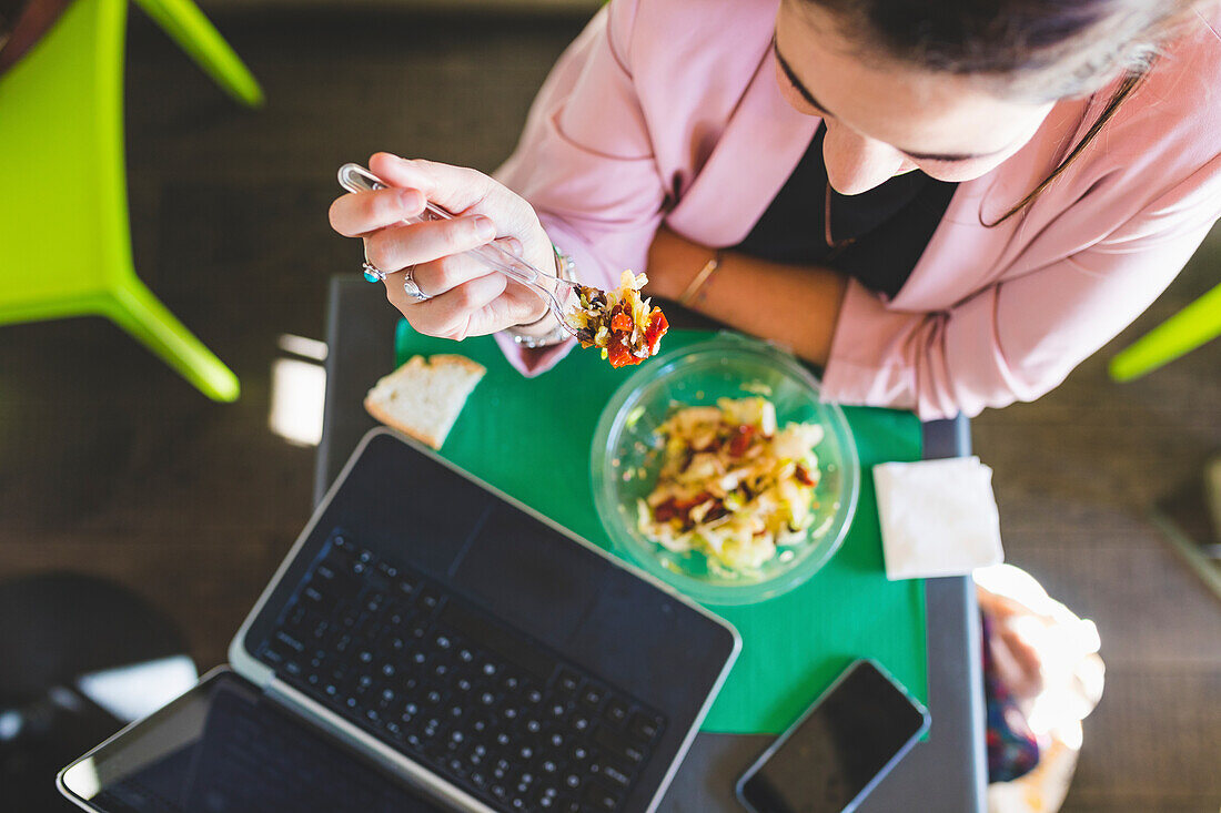 Young businesswoman having healthy lunch and using laptop