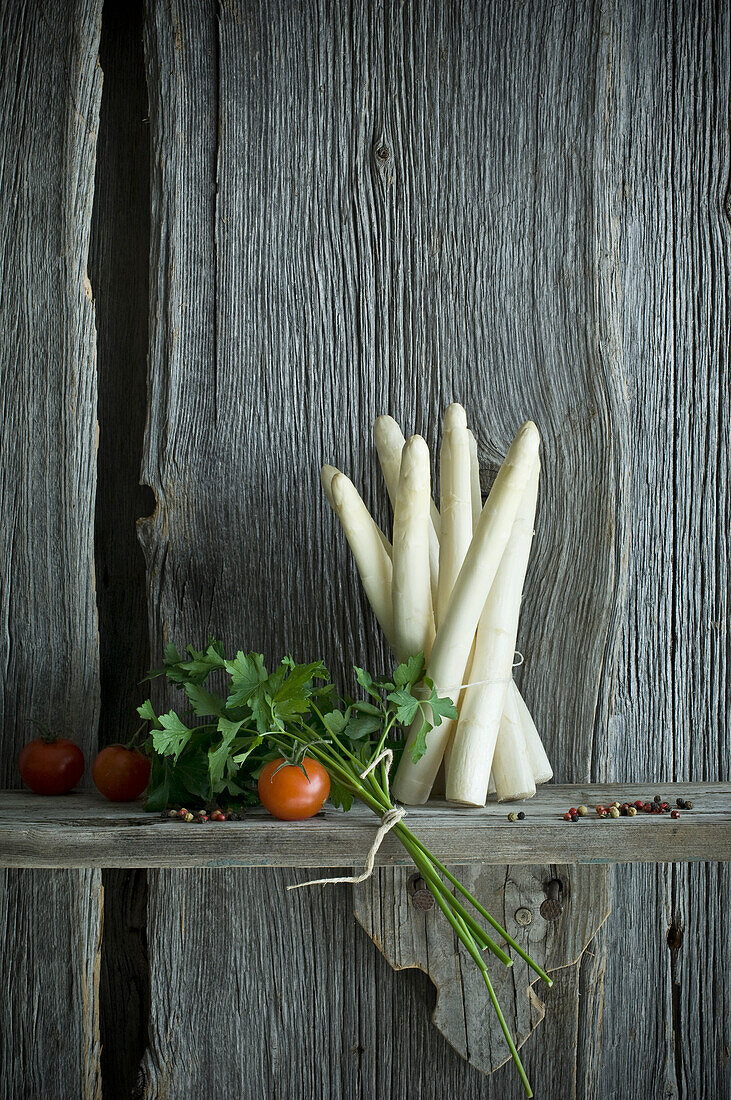 Bundle of white asparagus, tomato, parsley and mixed pepper on wood