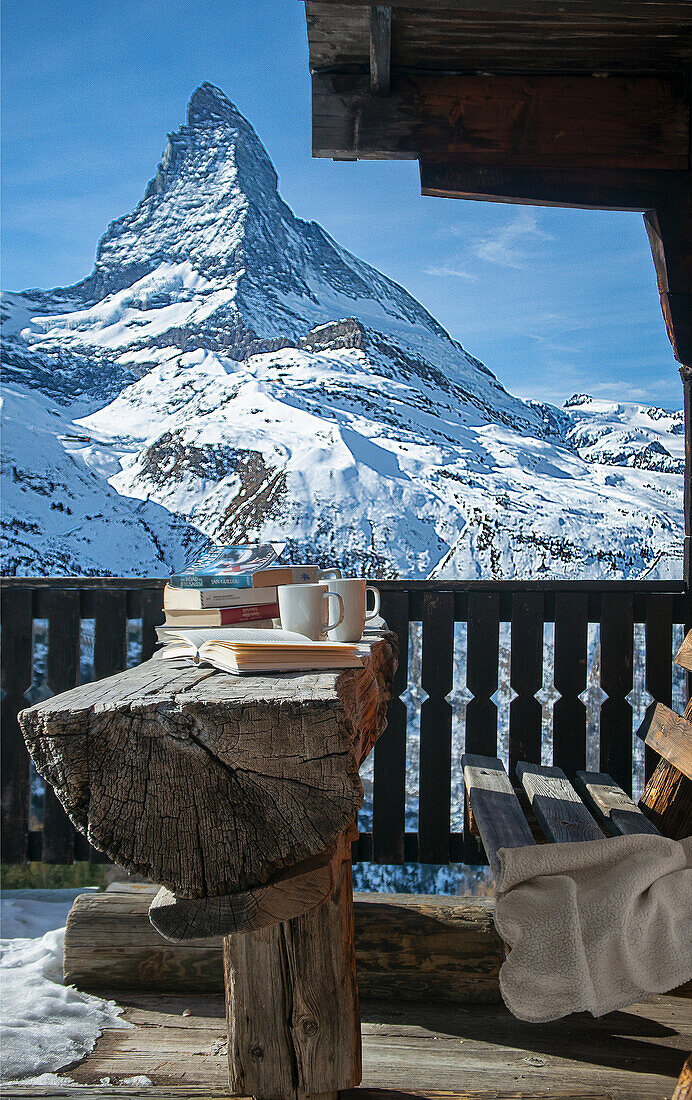 Blick auf schneebedecktes Matterhorn, Bank aus Holz, Tisch aus halbem Baumstamm, Bücher und Kaffeetassen