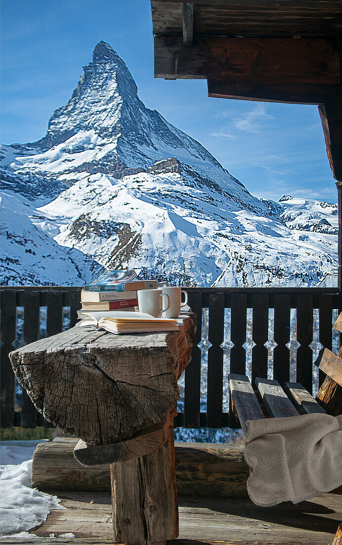 View of snow-capped Matterhorn, wooden bench, half-trunk table, books and coffee cups