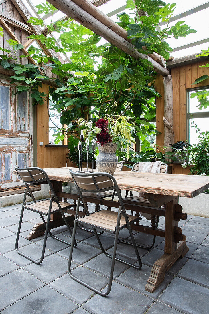 Holztisch mit Stühlen auf recycltem Fliesenboden in ehemaliger Scheune mit Glasdach