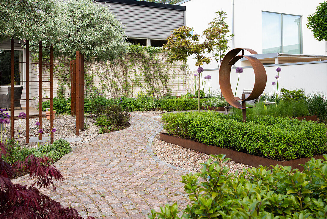 Garden path made with paving stones, bordered flower bed, and rusted metal sculpture