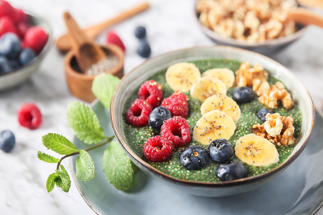 Buddha Bowl mit grünem Chia-Pudding mit Bananenscheiben, Heidelbeeren, Himbeeren und Walnüssen