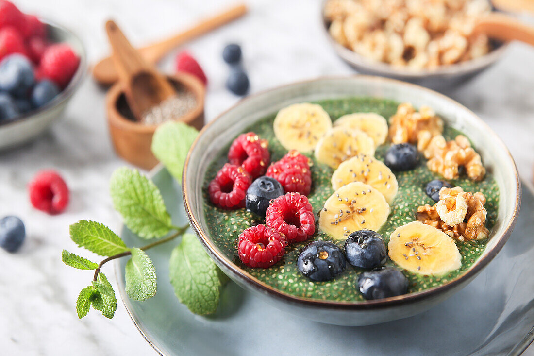 Buddha bowl of green chia pudding with slices of banana, blueberries, raspberries and walnuts