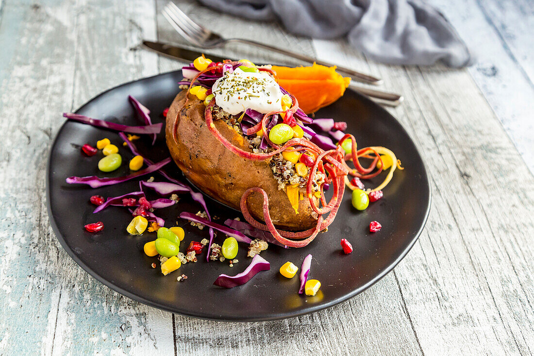 Kumpir, gefüllte Süßkartoffeln, Rotkohl, Mais, Edamame, Karotten, Quinoa, Creme Fraiche auf Teller