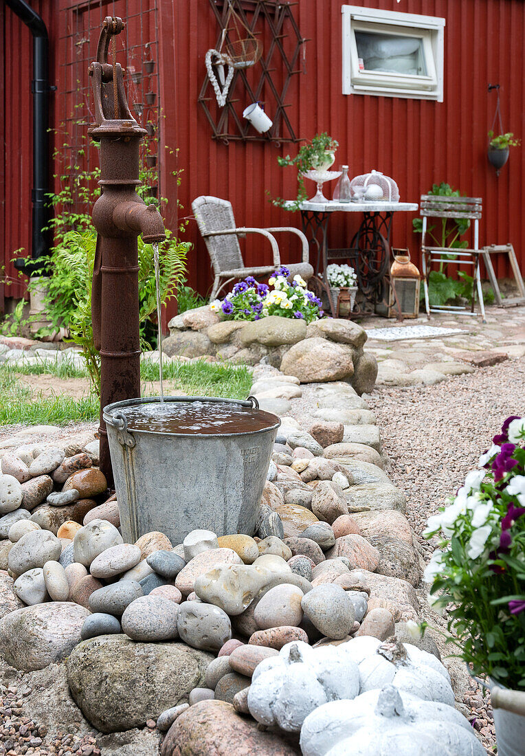 Wasserspiel aus rostiger Wasserpumpe und altem Eimer zwischen Steinen