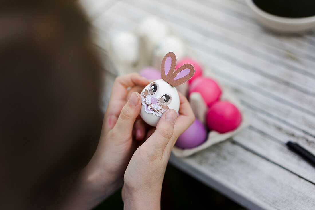 Close-up of girl decorating Easter egg on garden table