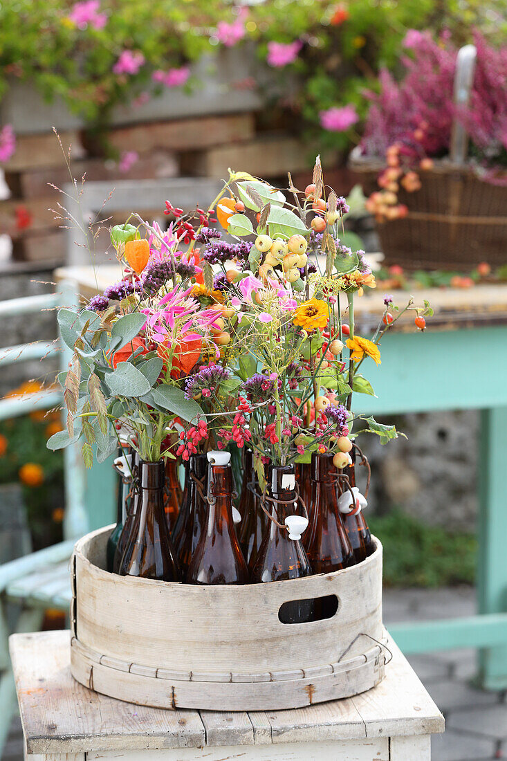 Zinnien, Waldreben-Fruchtstände, Salbei, Wasserdost, Physalis und Beerenzweige in Flaschen