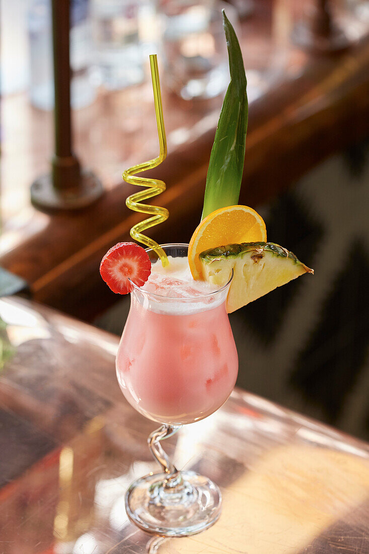 A pink cocktail, garnished with strawberry, orange and pineapple