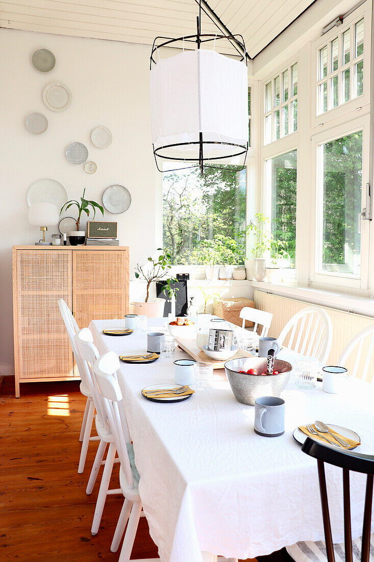 Brightly furnished dining room with white dining table, rattan chest of drawers and Asian pendant light