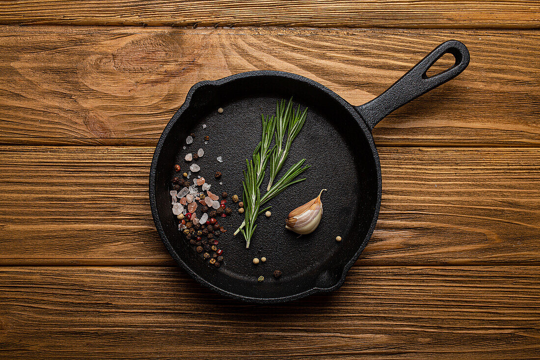 Black cast iron frying pan skillet with fresh rosemary, garlic, salt and pepper